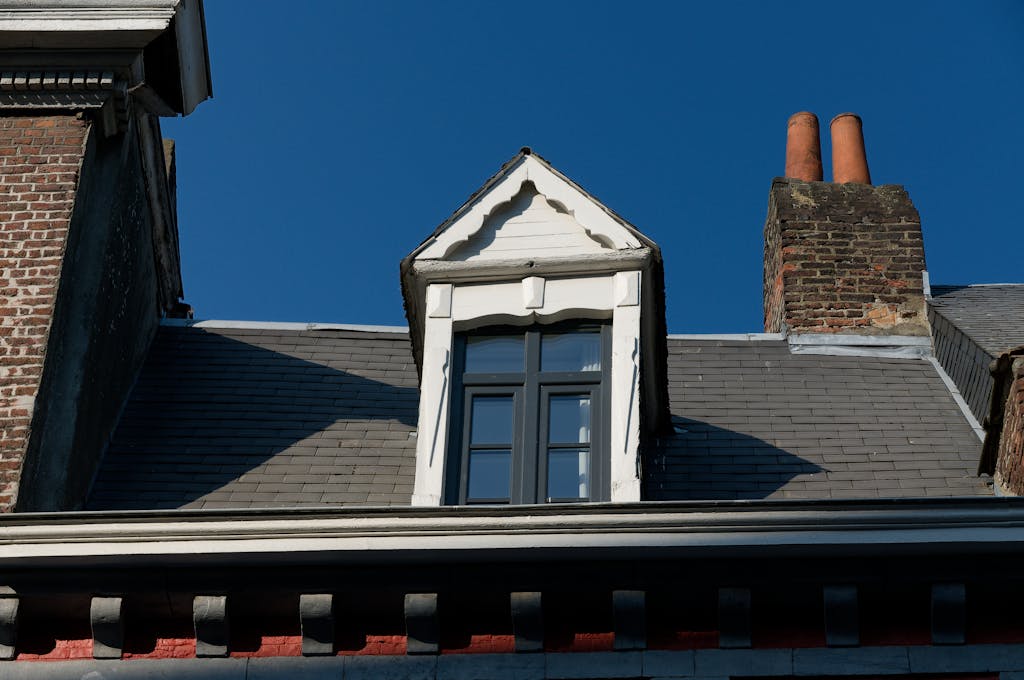 A stunning architectural detail of a rooftop with a window and brick chimney under a clear blue sky.