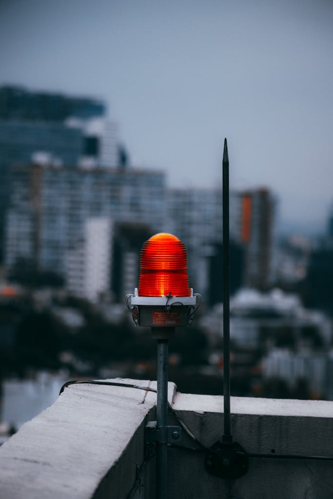A vibrant red warning light on a city rooftop against a blurred urban skyline at dusk.