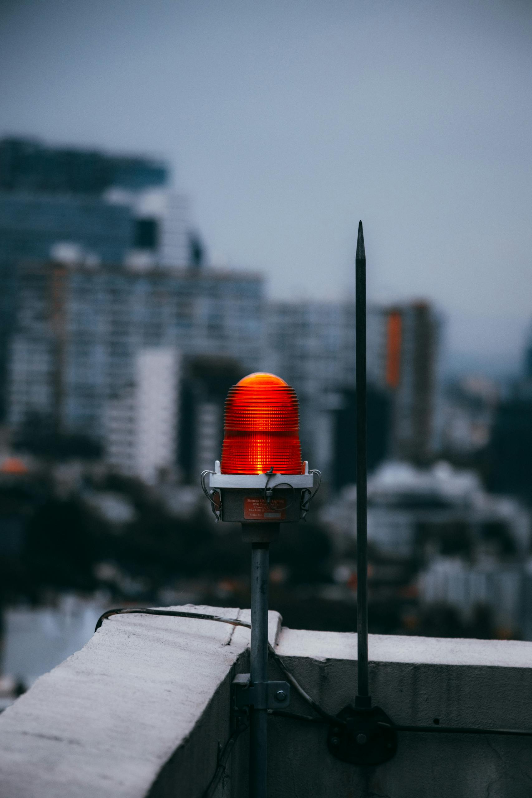 A vibrant red warning light on a city rooftop against a blurred urban skyline at dusk.