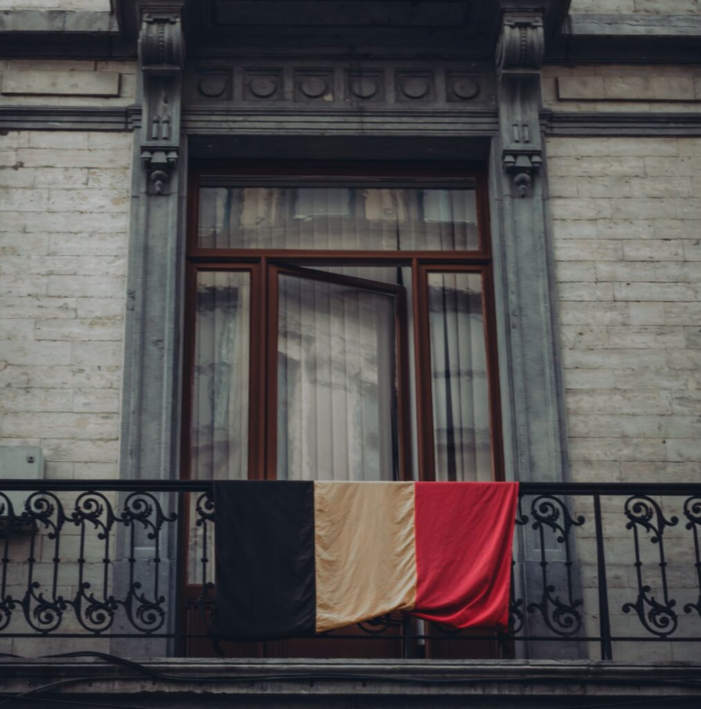Close-up of historic building facade with Belgian flag draped on the balcony.