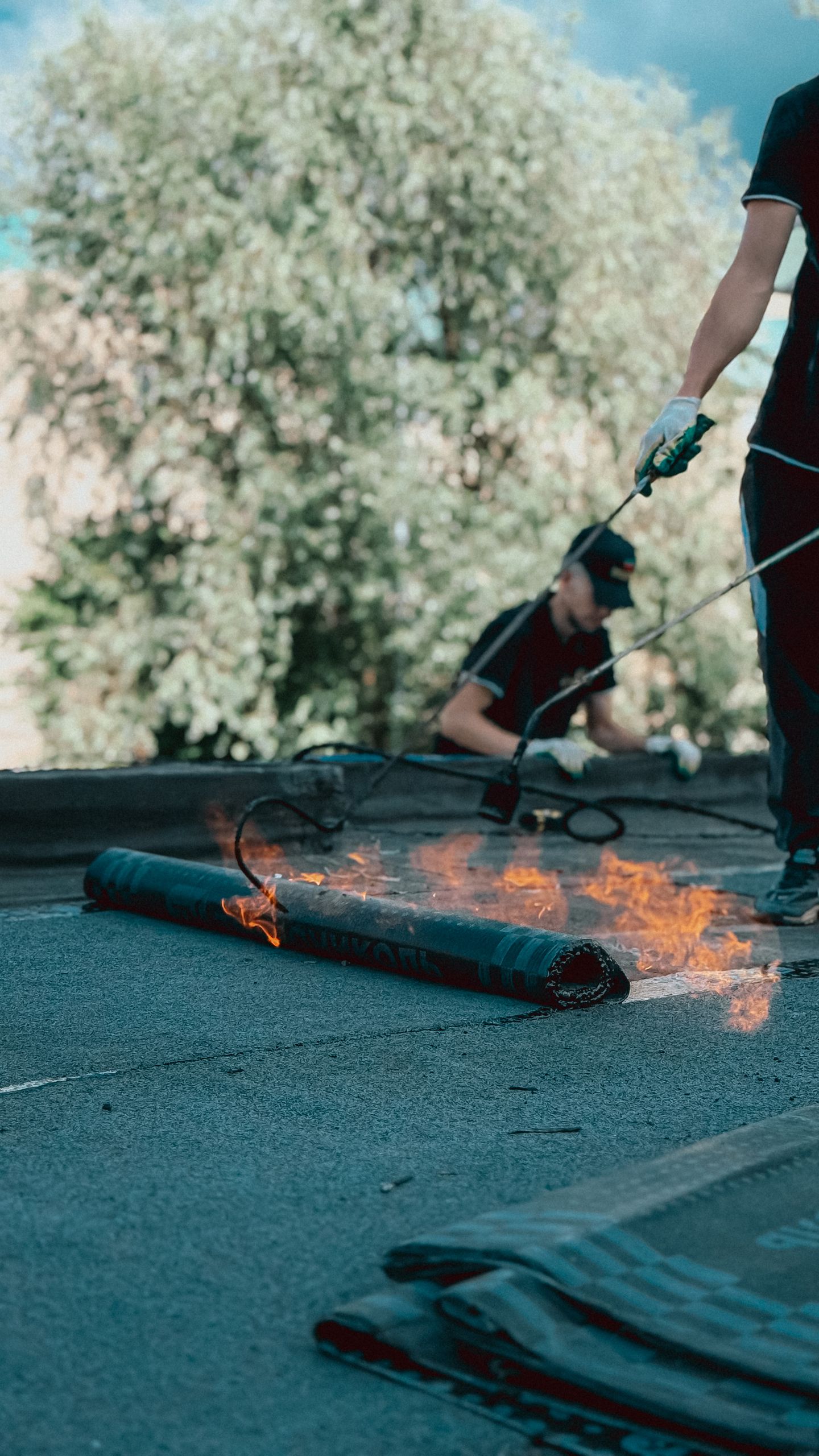 Roofers applying torch down rubber membrane for waterproofing. Outdoor construction scene highlighting skilled labor.