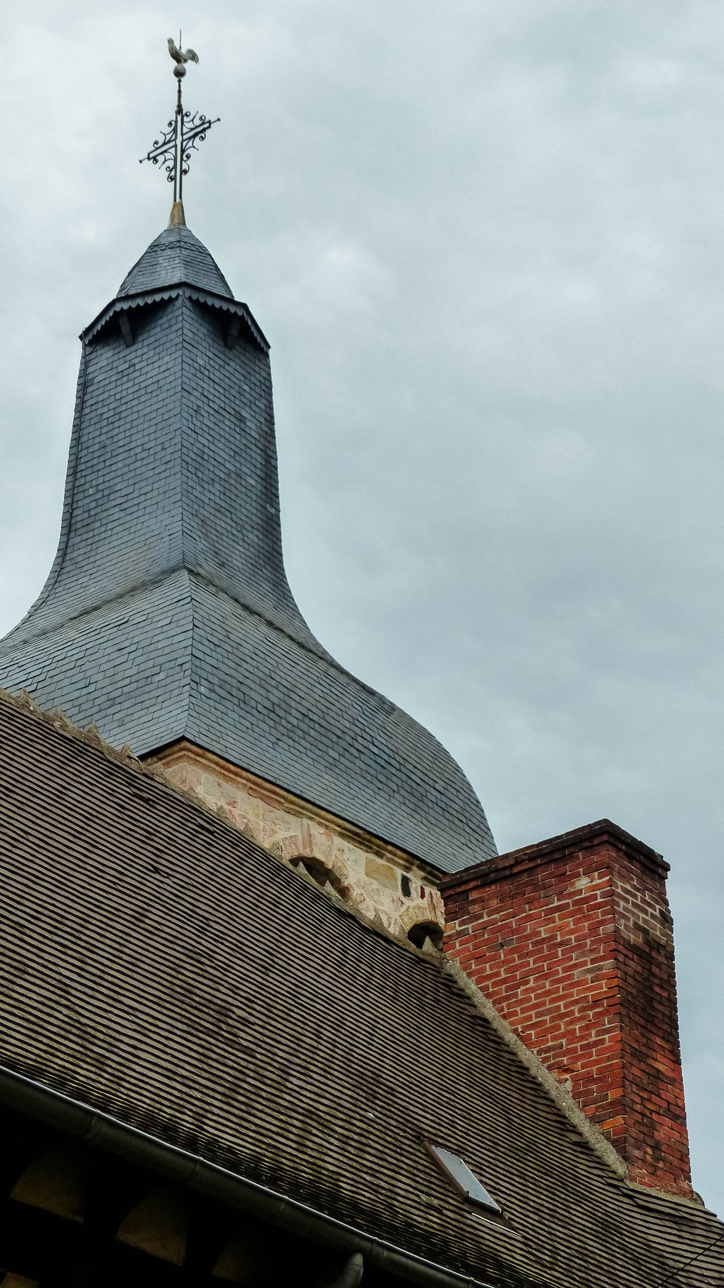 Vertical shot of a church tower in Montluçon, France, under overcast skies.