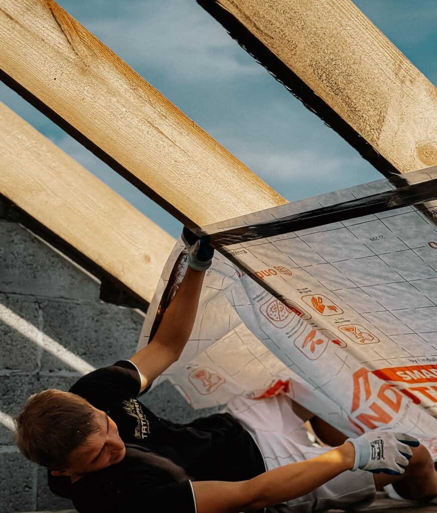 Young construction worker installing insulation on a roof during daylight. Captured outdoors with natural lighting.